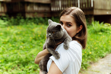 a cute girl gently hugs a cat while being outside. cat in hand. pet care. domestic scottish gray...