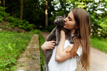 a cute girl gently hugs a cat while being outside. cat in hand. pet care. domestic scottish gray cat. walk with the cat