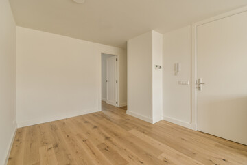 an empty room with white walls and wood flooring on the right side, there is a door that leads to another room