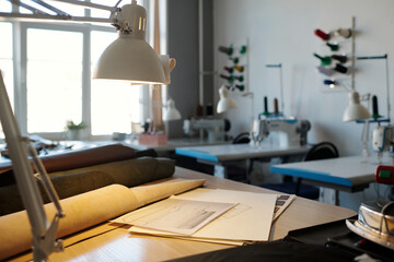 Focus on workplace of leatherworker with lamp, sketches and rolled leather textile of various colors against desks with sewing machines