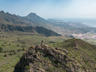 Drone shot of a young boy on the top of a mountain  with huge mountains in the background