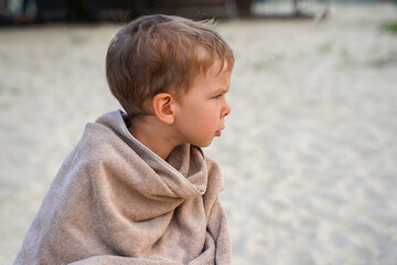 A little boy sits on the beach, wrapped in a towel and watches his younger brother vigilantly. Safety on the water. Family support