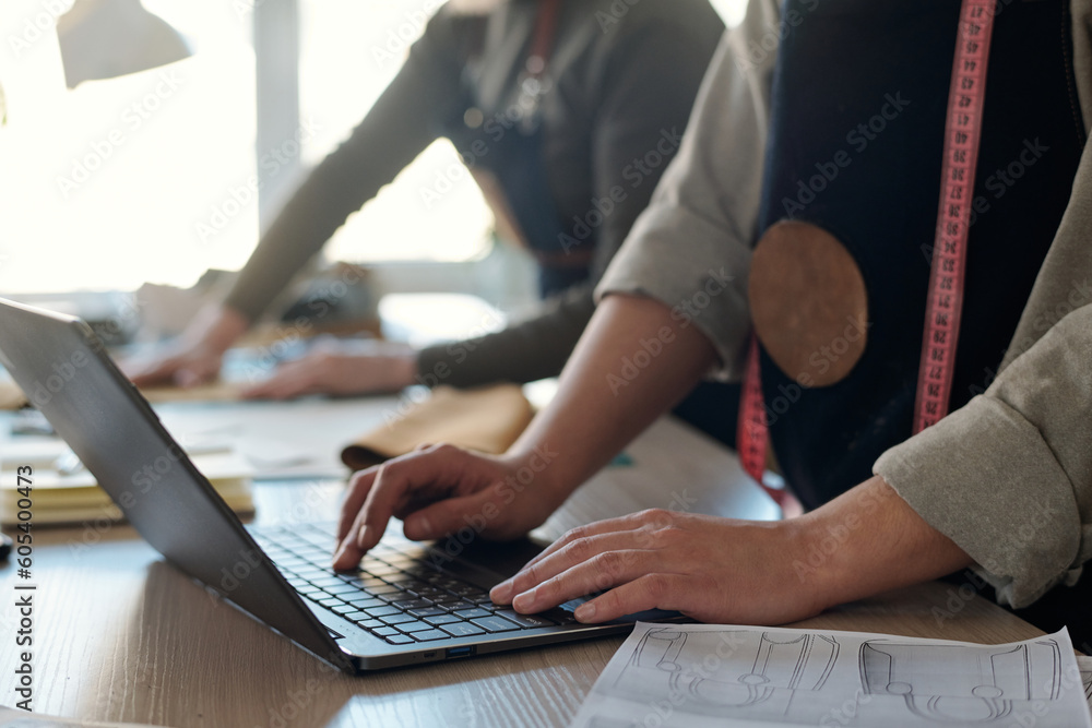 Poster close-up of young craftswoman pressing keys of laptop keyboard while standing by workplace and check