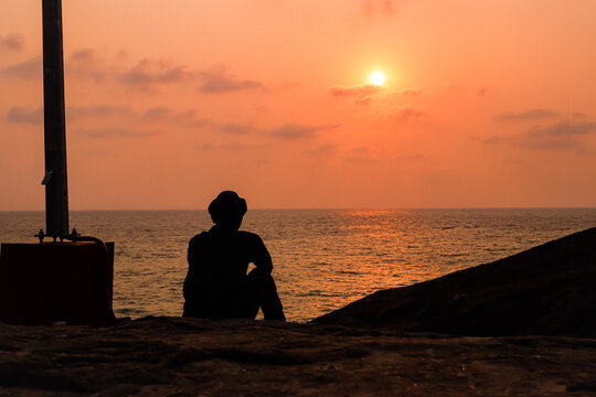 the silhouette image of a sad young boy sitting near an ocean