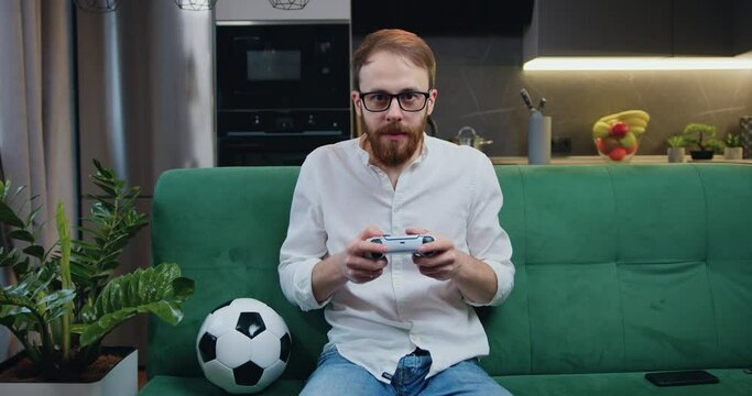 Focused man playing video game in moderm kitchen apartment enjoying indoor activity. Online entertainment and leisure activity concept.