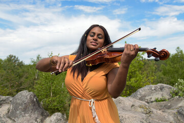 Lovely black woman playing violin in the forest