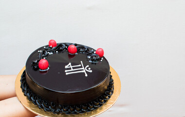 Beautiful Chocolate truffle cake topped with red cherry written "Maa" in hindi means mother in white background. Concept of giving thanks or birthday or mother's day or any occasion of mom. copyspace