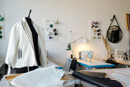 New white leather jacket on mannequin and workplace of tailor or leatherworker with spools of threads on wall and sewing equipment