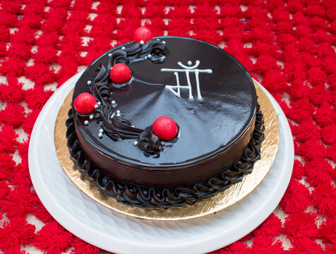 Beautiful Chocolate truffle cake topped with red cherry written "Maa" in hindi means mother in red background. side view . Concept of giving thanks or birthday or mother's day or any occasion of mom. 