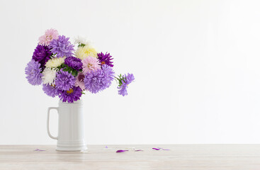 beautiful bouquet of asters in white jug on background white wall
