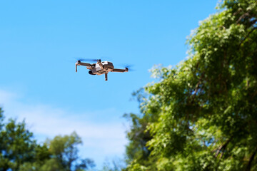 Fototapeta na wymiar A small photography quadcopter drone flies over the trees in the sky. Modern electronic and photo and video devices