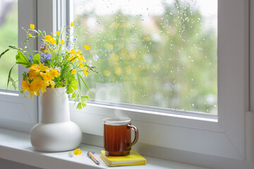 summer flowers in white jug with cup of tea on windowsill