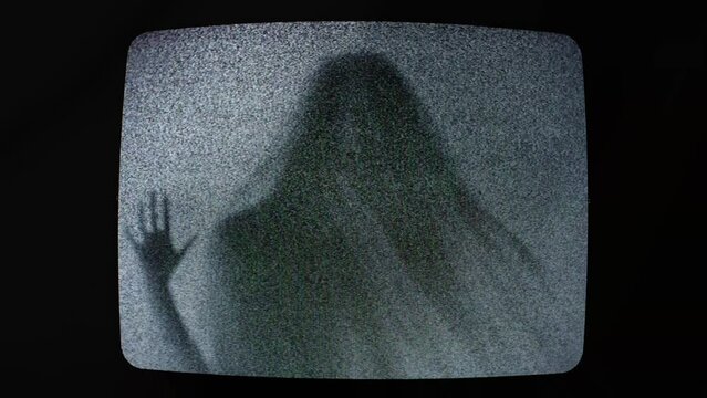 The ominous scary silhouette of a veiled ghost trapped inside an old retro analog television, touching the screen, struggling to escape, mixed with static noise.
