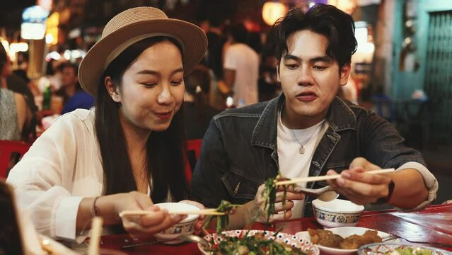 Young Asian couple traveler tourists eating Thai street food together in China town night market in Bangkok in Thailand