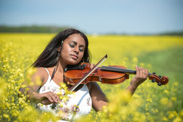 Lovely black woman playing violin in a rapeseed field
