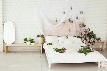 beautiful bright room in boho style with a large bed covered with a white bedspread and decorated with lilac flowers