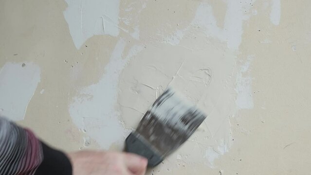 A man is plastering a damaged wall in a room with a hand trowel.