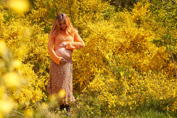 Woman enjoying pregnancy, smile, relaxing, hugging belly. Pregnant woman looking and holds hands on belly outdoor.Pregnancy, maternity, preparation and expectation concept.