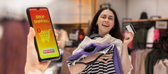 Web banner of drop shipping. Happy young woman holds hangers with clothes and bank card. Close up...