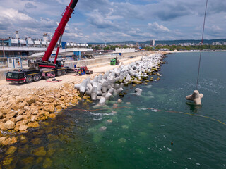 Aerial view of breakwater construction. Bulldozer and crane on a pile of boulders in the sea