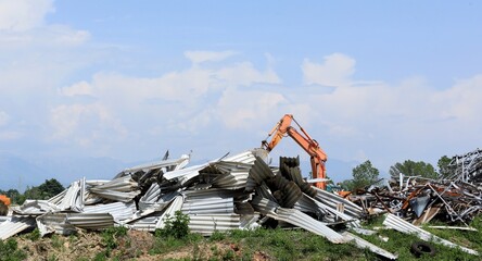 Large stack of aluminum and ferrous materials scrap in the recycling center. Orange excavator boom behind it.