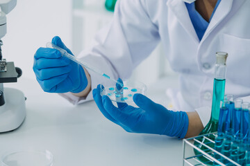 medical or scientific researcher researching and experimenting Multi-colored solution, vial and microscope In the laboratory or in the laboratory by wearing blue gloves and white clothing completely.