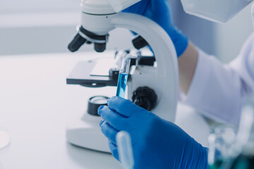 medical or scientific researcher researching and experimenting Multi-colored solution, vial and microscope In the laboratory or in the laboratory by wearing blue gloves and white clothing completely.