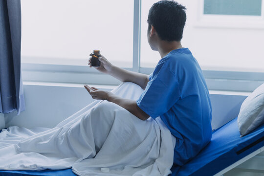 Asian Male Patient Lying On Bed With Face Mask In Recovery Room In Hospital Ward. All People Wearing Mask To Prevent Covid19 Virus Infection During Coronavirus Pandemic. The Man Feels Lonely And Bore.