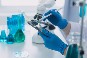 medical or scientific researcher researching and experimenting Multi-colored solution, vial and microscope In the laboratory or in the laboratory by wearing blue gloves and white clothing completely.