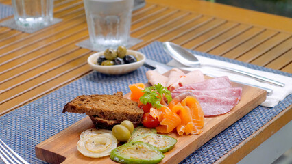 Wooden cutting board with meat and vegetables, cold cuts in restaurant. Smoked salmon, salami, rye bread and grilled vegetables on lunch in outdoor cafe.