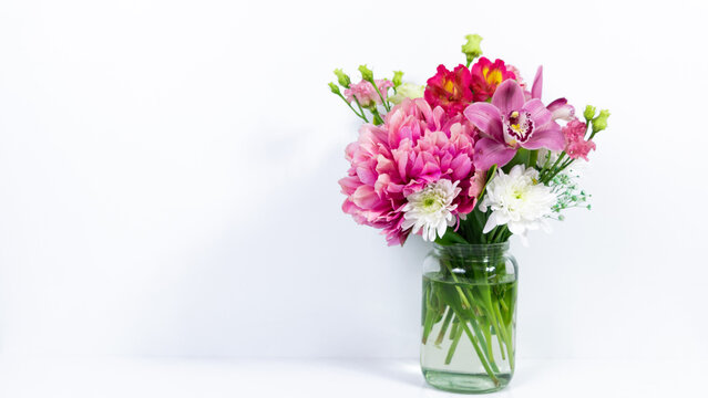 Bouquet of various natural flowers in a glass jar on a white background.