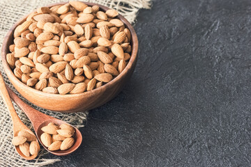 almond seeds in a large wooden bowl and spoons on the table close-up. almond background and a copy space.