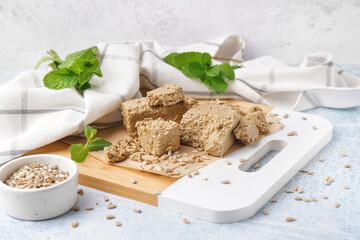 Board with pieces of tasty halva and sunflower seeds on light background