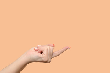 The hand of a young girl on a beige background. Holds a thumbs up.