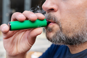 Habit concept, a man smokes an electronic cigarette. Hipster man holding a vaping device. Health...