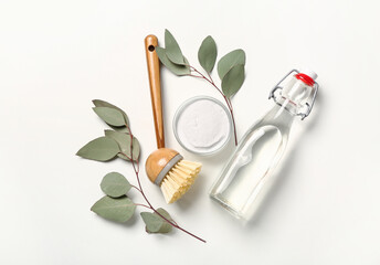 Bottle of vinegar, bowl with baking soda, cleaning brush and eucalyptus branches on white background