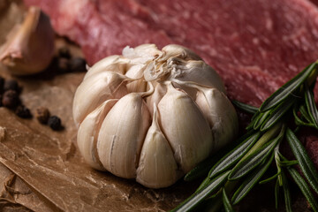 Raw steak on wooden cutting board with garlic, pepper and rosemary.