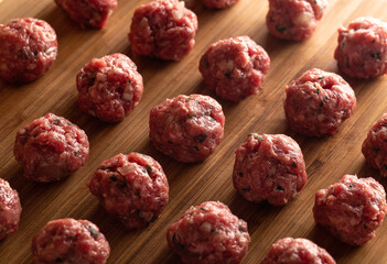 Raw uncooked meatballs on wooden cutting board.