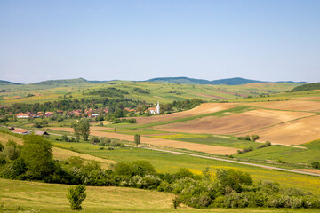 Small szekler village among green hills, blue sky in the spring. East European villages - Transylvania region