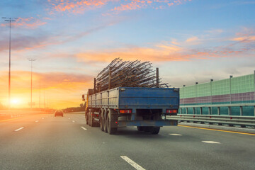 Truck with long trailer loaded with metal cylinder rebar frame for the construction of a building drives along the highway. - obrazy, fototapety, plakaty