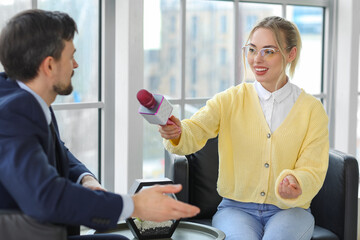 Female journalist with microphone having an interview with man in office