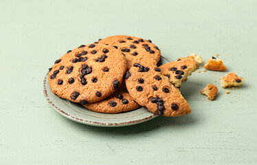 Plate of tasty cookies with chocolate chips on green wooden background