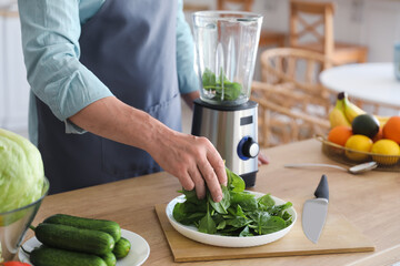 Mature man making smoothie with spinach in kitchen, closeup