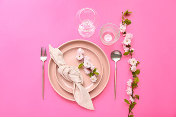 Beautiful table serving with cutlery, blooming tree branches and folded napkin on pink background
