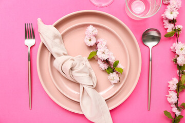 Beautiful table serving with cutlery, blooming tree branches and folded napkin on pink background