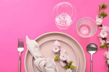 Beautiful table serving with cutlery, blooming tree branches and folded napkin on pink background