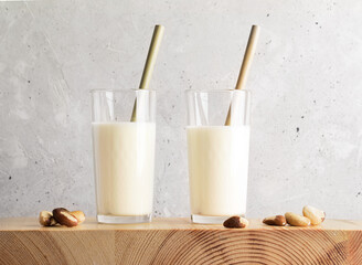 Vegan milk made of brazil nut in two glass with bamboo drinking straws and nuts on wooden table.