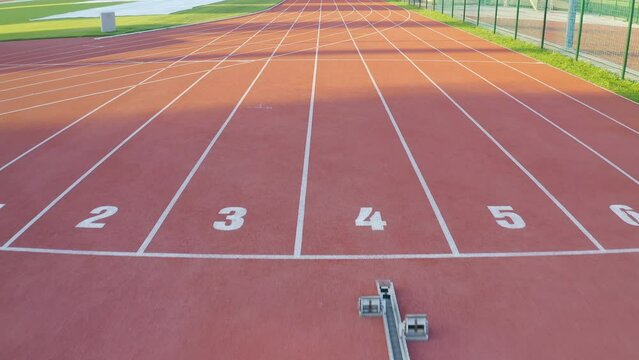 Starting block and starting line of the red tartan athletic track with eight lanes, drone tracking shot.