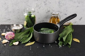 Saucepan with fresh cucumbers and ingredients for preservation on table