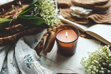 Burning candle and bouquet of lilies of the valley, aesthetic home atmosphere